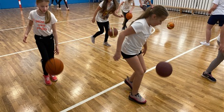 Powiększ grafikę: Uczniowie z klasy 4A/B kozłują piłkę od koszykówki podczas rozgrzewki.