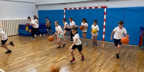 Powiększ grafikę: Uczniowie z klasy 5A kozłują piłkę od koszykówki podczas rozgrzewki.