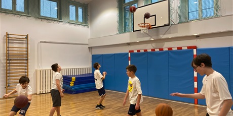 Powiększ grafikę: Klasa 7A rozgrzewająca się z piłkami od koszykówki na sali gimnastycznej.